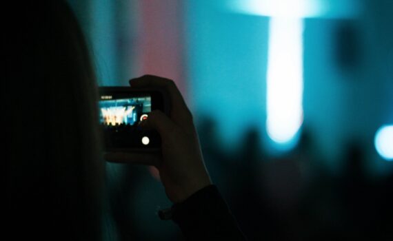 Foto Veranstaltungsteilnehmer fotografiert oder filmt mit Smartphone Bühne mit großem Lichtkreuz