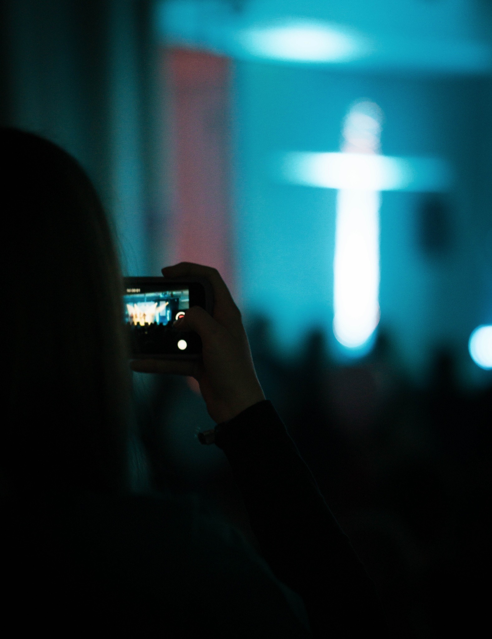 Foto Veranstaltungsteilnehmer fotografiert oder filmt mit Smartphone Bühne mit großem Lichtkreuz